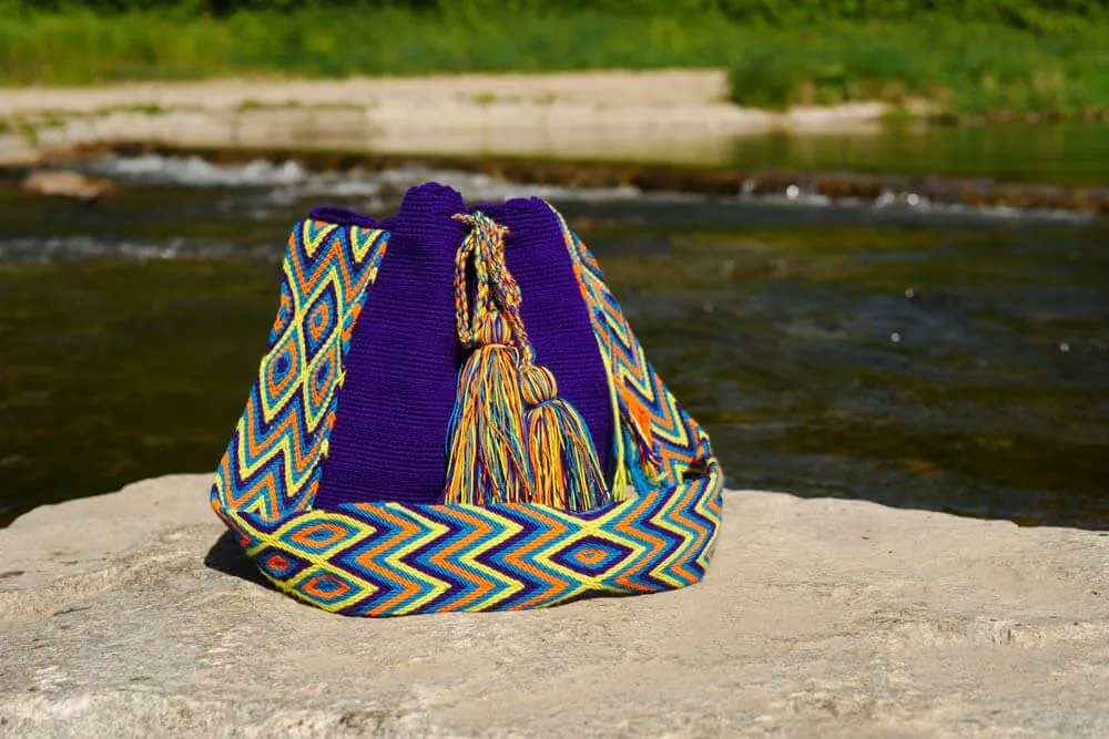 Lila Mochila Wayuu mit Zickzackriemen auf einem Stein am Fluss